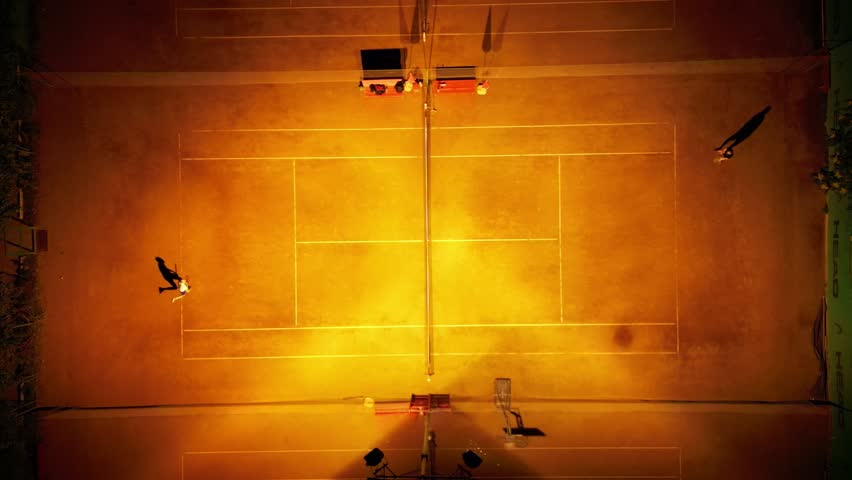 Tennis players practicing filmed from above on a clay orange red court. Well lit outdoor clay court with people playing seen from the top shot. High angle drone footage of sports competition