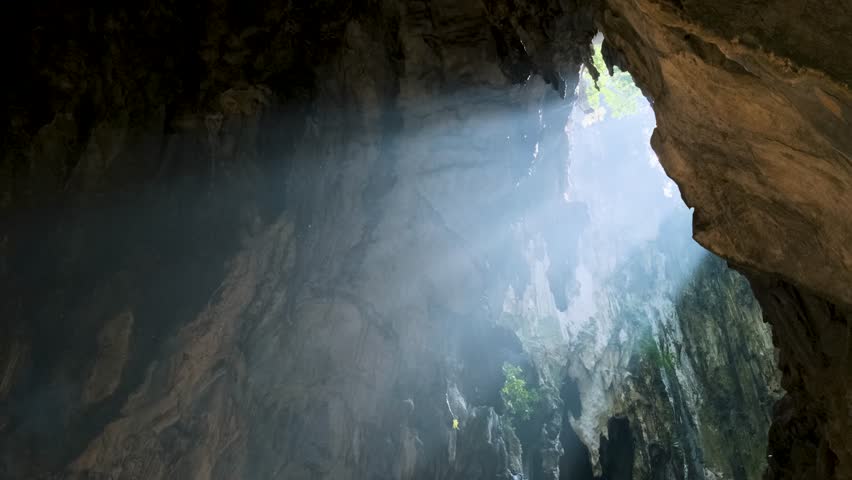 Sunlight streaming through Batu cave opening, illuminating the rugged rock formations and casting a mystical glow, creating a serene and mysterious atmosphere, Kuala Lumpur, Malaysia