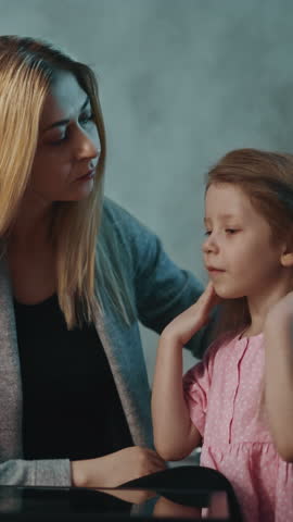 Careful mother touches forehead of cute little daughter to check temperature at small table with pill bottle in darkened room at home slow motion