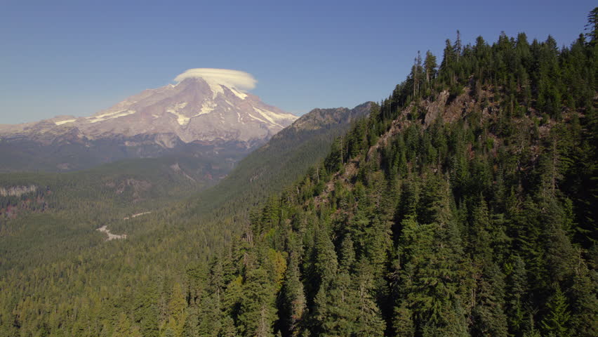 Aerial view of Mount Rainier with cloud formations and a lush forest in the foreground, Washington State, USA