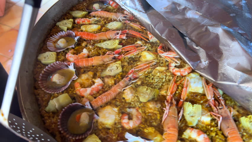 Plating a traditional Spanish seafood Paella dish with shrimps, St Jacques scallops and Cigala Norway lobsters Nephrops norvegicus, cooked rice with seafood, Marbella Spain, 4K shot