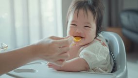 Closeup of Happy asian baby girl eating first food pumpkin from spoon with mom at home, Smile baby looking at camera. - Powered by Shutterstock - Get 15% off with code: PIKWIZARD15