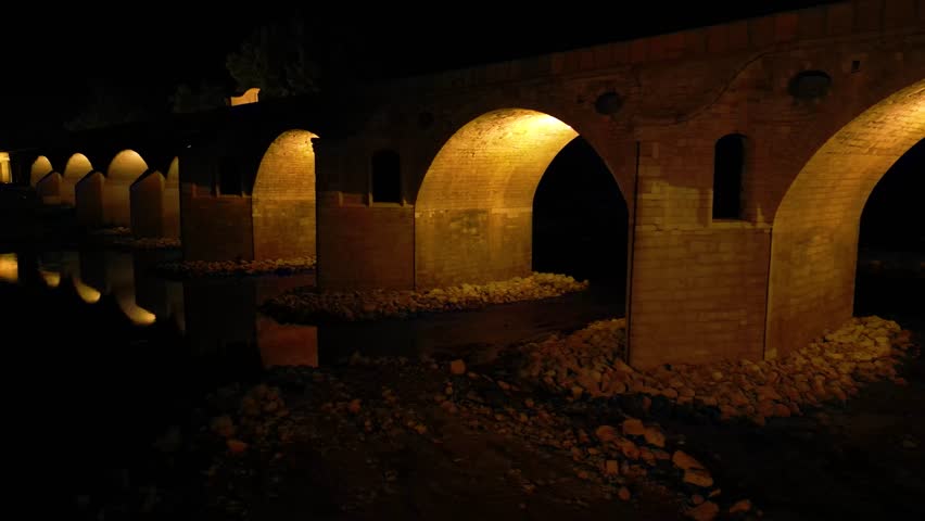 Aerial high angle footage of a 150 years odl stone masonry bridge illuminated on a dark night. Drone shot of Master Kolyo Fitcheto