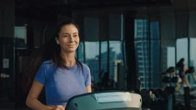 Young sportswoman with earphones runs on treadmill in gym. Happy brunette woman shows dedication and energy during cardio training. Sports club with inspiring workout atmosphere - Powered by Shutterstock - Get 15% off with code: PIKWIZARD15