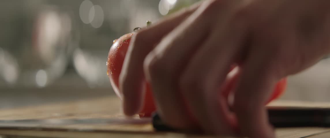 Close-up of a chef cutting a red tomato with a knife on a wooden board. Slicing a tomato with a knife. Cutting vegetables, Culinary show cinematic footage slow motion