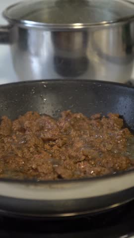 Red spatula stirring ground meat in a non-stick frying pan on the stovetop during cooking.