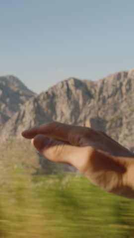 Vertical video. Hand Reaching Out of Car Window, Rocky Mountains Reflecting in Mirror, Capturing the Thrill of High Mountain Travel and Expansive Views in Motion.