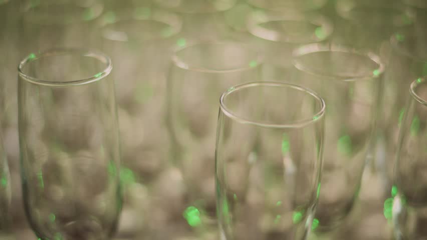 Multiple party empty glasses, colorful lights shining trough, close up shot hovering over