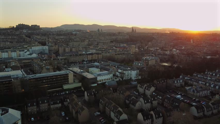 A stunning sunset over Edinburgh, showcasing the city’s architecture and urban landscape. Drone footage captures the Edinburgh Castle, residential areas, and hills, all illuminated by the sun.