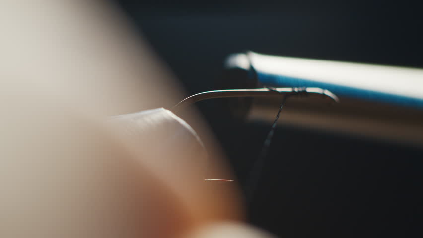 Person wraps thread around the hook during tying the fishing fly. Macro studio footage of the fishing fly tying process