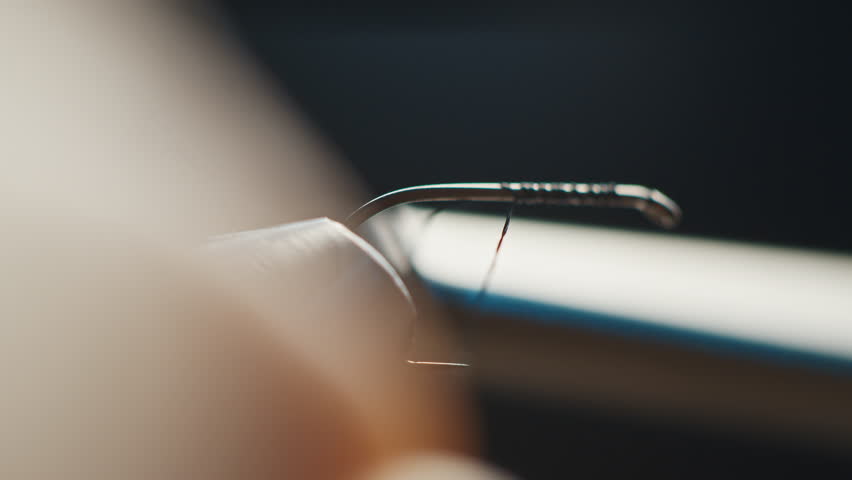 Person wraps thread around the hook during tying the fishing fly. Macro studio footage of the fishing fly tying process