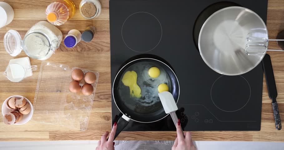 Cooking eggs in frying pan on kitchen stove. Break egg yolk in frying pan