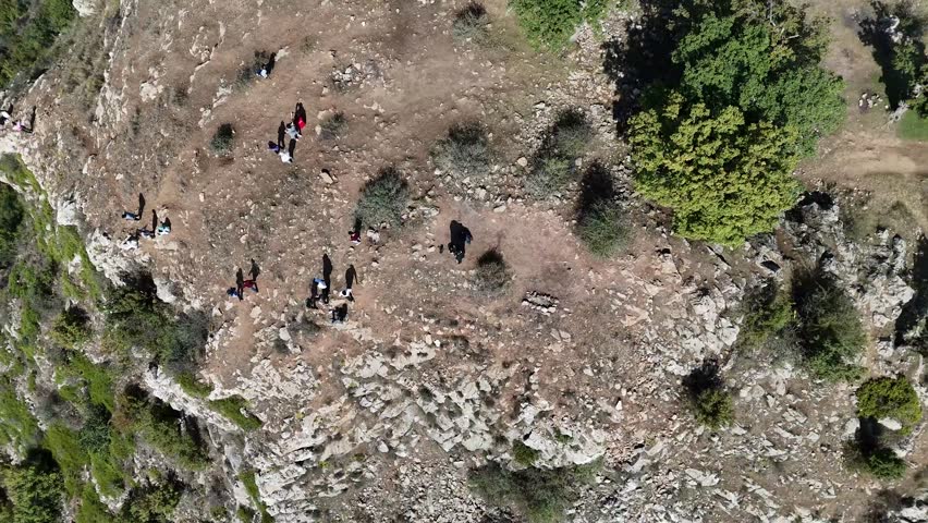 Upward movement of the camera showing the shadows of people on top of a rock in the forest and watching cars in the woods.
