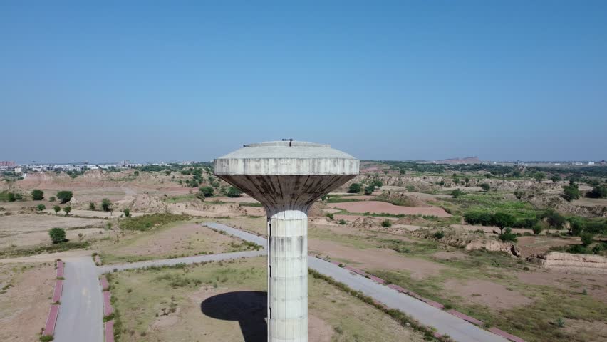 A drone view of concrete water tower in a sunny day with blue sky and empty land