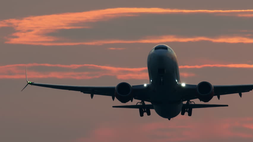 Airplane seen from below as it takes off during sunset with the sky illuminated in soft orange hues, highlighting the silhouette of the aircraft - captured in slow motion