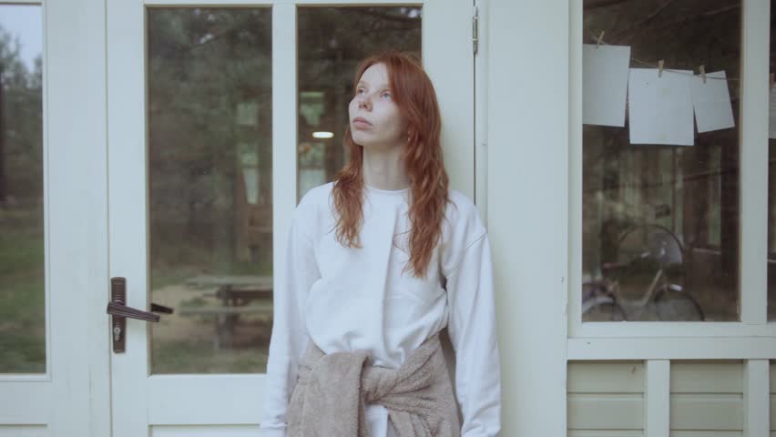 A young Caucasian woman enjoying the fresh air while standing on the veranda 