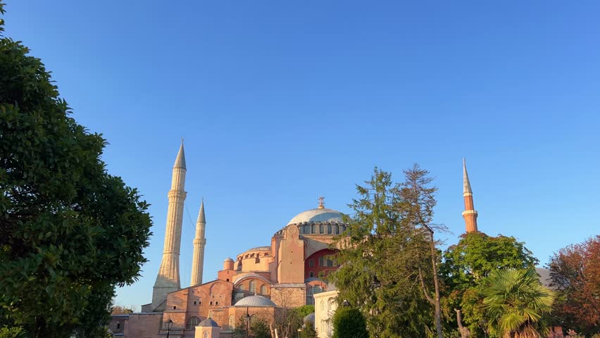 ISTANBUL, TURKEY - JULY 15, 2024: The beautiful Hagia Sophia and the fountain with trees and flower beds in the park. The Christian Patriarchal Basilica, the Imperial Mosque against the blue sky. 4K