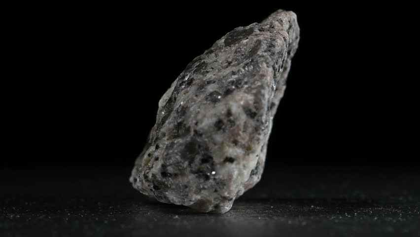Granite (igneous rock containing silica and quartz) small sample rotating slowly against a black background [UK]