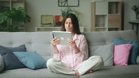 Woman relaxes on a cozy couch, using a tablet in a bright living room with modern and cozy decor elements. 4K video, slow motion, 50 fps - Powered by Shutterstock - Get 15% off with code: PIKWIZARD15