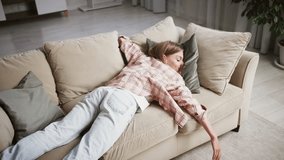 Young woman in casual attire collapsing onto a sofa, showcasing exhaustion after a demanding day. The scene captures a moment of relaxation and tranquility in a cozy living room - Powered by Shutterstock - Get 15% off with code: PIKWIZARD15