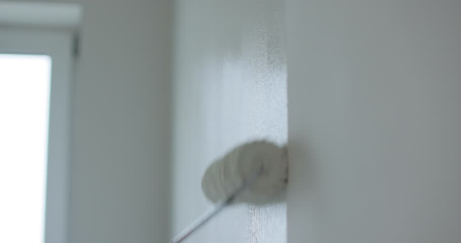 Man painter painting a house wall with a white paint roller. Painting and repair of the premises.
