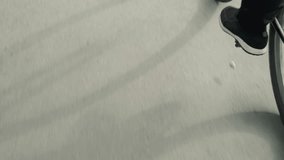 Close-up of someone pedaling bicycle slowly, with detailed view of sneakers and black trousers, casting a distinct shadow of the bike and rider on the sunlit pavement - Powered by Shutterstock - Get 15% off with code: PIKWIZARD15