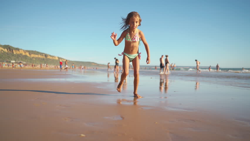 Cheerful wet girl running on sandy beach against clear blue sky during sunny day. Female child in swimwear is spending leisure time during vacation 