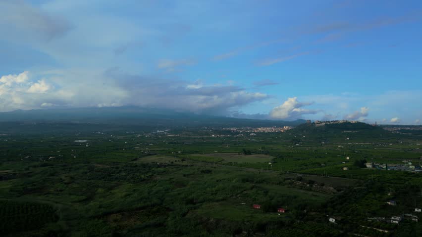 Aerial pull-back view of the town of Paternò in Sicily with Mount Etna in the background and orange groves