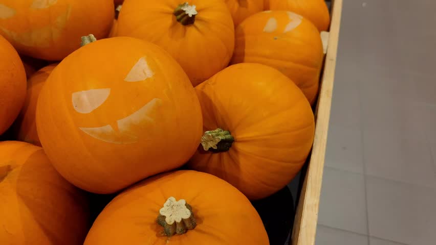 Pan shot of Halloween pumpkins with scary faces that lie in a wooden basket in a supermarket for decoration and to be sold