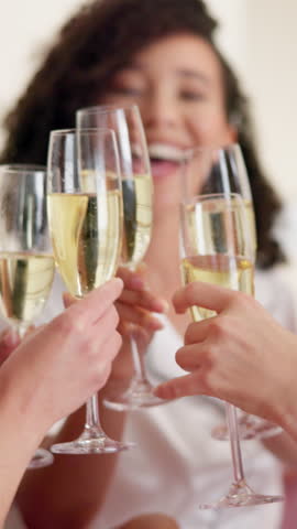 Cheers, champagne and bride with friends in hotel for getting ready for marriage ceremony. Happy, alcohol drink and woman with bridesmaids with sparkling wine for toast at wedding location together.
