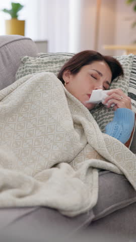 Sick, woman and blowing nose for cold, flu and illness with blanket for wellness and comfort on living room sofa. Girl, sneezing and recovery for health, virus or allergy with rest and relax in house