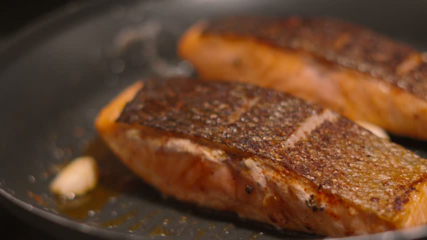 Salmon Fish Fillets Cooking in Frying Pan with Crispy Skin with Oil, Butter and Garlic Cloves. Food Preparation Ready to Serve Lunch or Dinner 4K