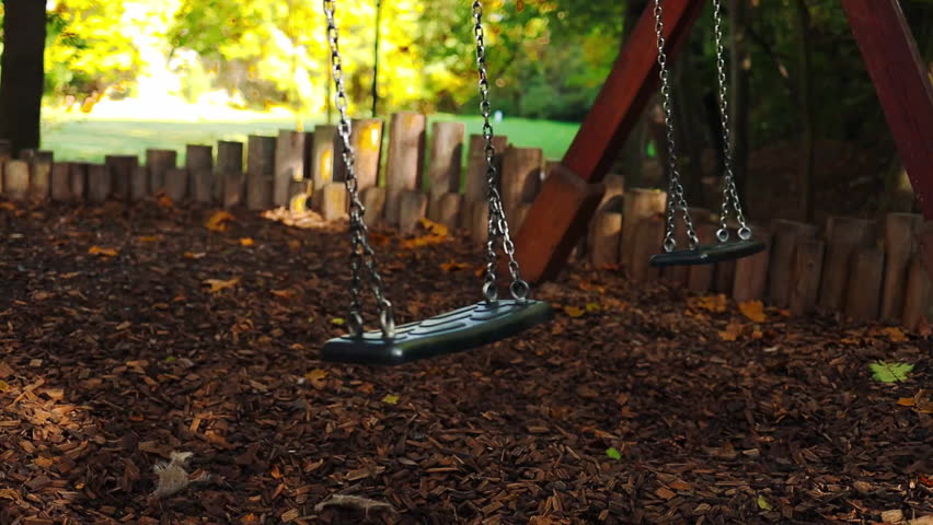 Empty black swing on children playground in the park in autumn season. Missing child. Lonely swing in sunny autumn day. Golden foliage in late fall. Beautiful nature. High quality FullHD footage