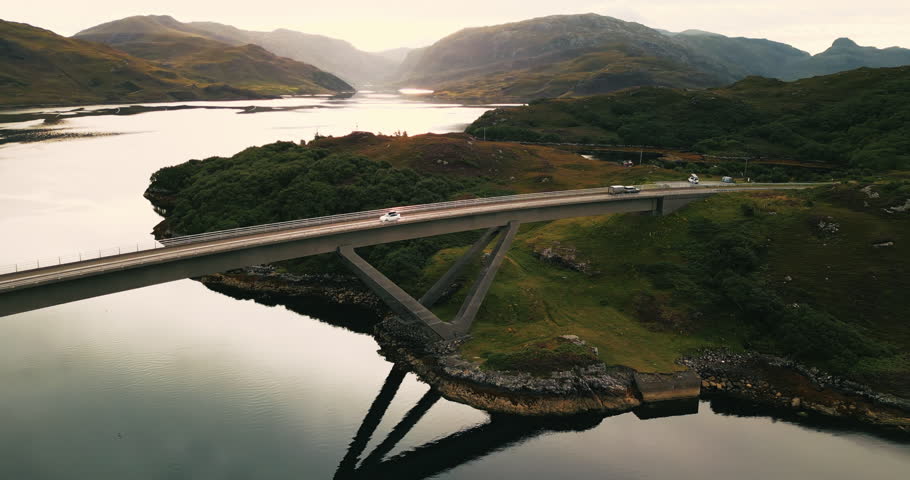 Epic view from above of white traveler car driving on iconic Kylesku Bridge with sunny Scottish landscape
