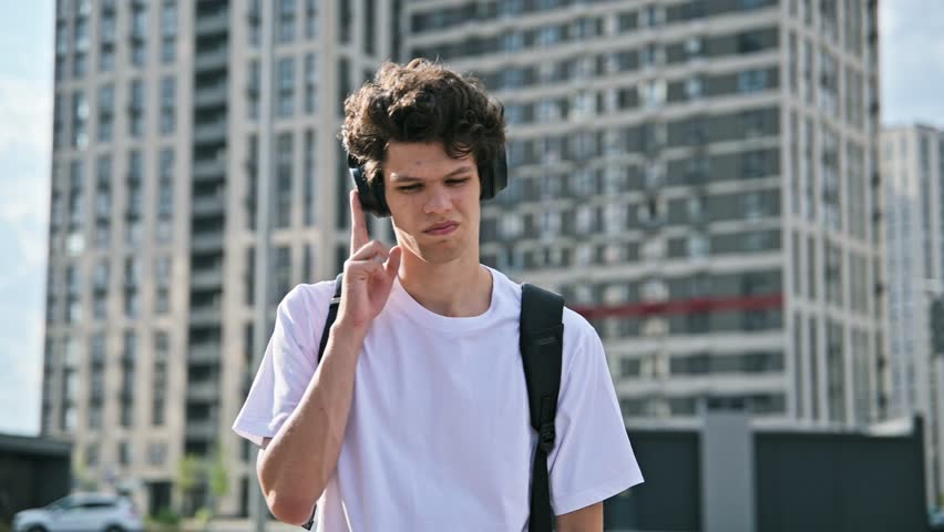 Young serious man in headphones listening to audio, outdoors