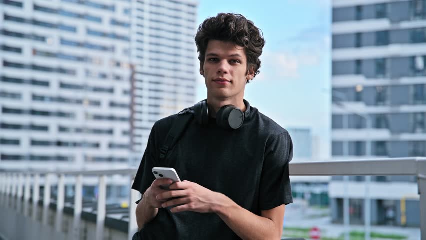 Handsome young male with backpack smartphone, looking at camera outdoor