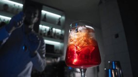 Bartender at the bar prepares a refreshing orange cocktail, a red cocktail with ice cubes and skillfully mixes it with a bar spoon. Close up. Slow motion - Powered by Shutterstock - Get 15% off with code: PIKWIZARD15