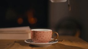 Close-up of a female hand pouring hot tea from a teapot into a cup, creating a cozy ambiance with a warm fireplace in the background. Concept of relaxation and warmth - Powered by Shutterstock - Get 15% off with code: PIKWIZARD15