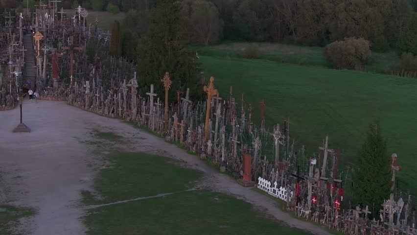 Aerial perspective of the Hill of Crosses in Lithuania, showcasing thousands of crosses and visitors amidst green fields.