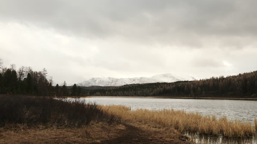 Hiker walks along a mountain lake surrounded by forest and hills, exploring nature and enjoying a peaceful scenic landscape outdoors.