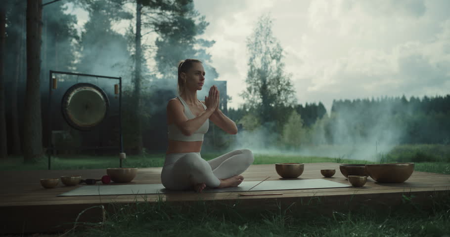 With a Gong in the Background and Trees Surrounding Her, Young Female Meditates on a Terrace, Incense and Singing Bowls Placed Nearby. Aromatic Scents and Peaceful Sounds Enhance the Mindfulness