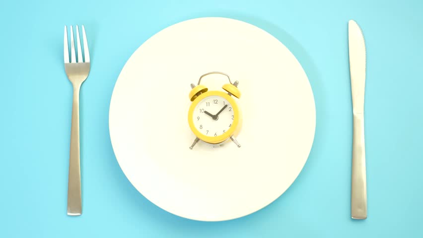 Empty plate with alarm clock on blue background, intermittent fasting concept.