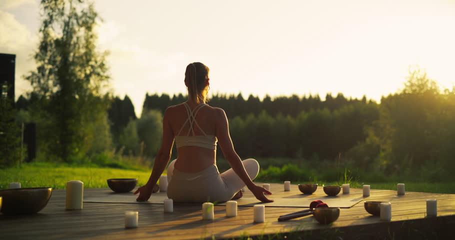Portrait of a Female Performing Yoga Amidst the Beauty of a Nature Retreat. Her Focus and Breath Aligning with Stretching Exercises. She is Sitting Between Singing Bowls and Incense Candles