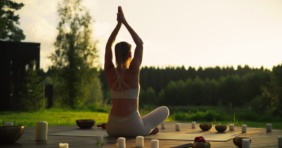 Portrait of a Female Performing Yoga Amidst the Beauty of a Nature Retreat. Her Focus and Breath Aligning with Stretching Exercises. She is Sitting Between Singing Bowls and Incense Candles
