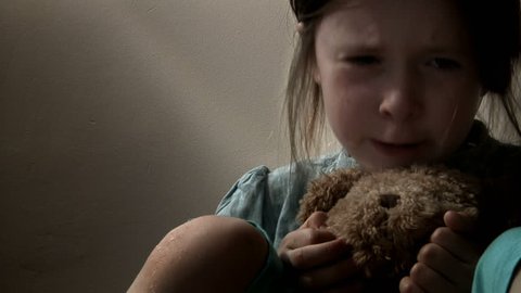 Little girl crying, with tears streaming down her face, clutching her teddy bear. Intentionally desaturated.