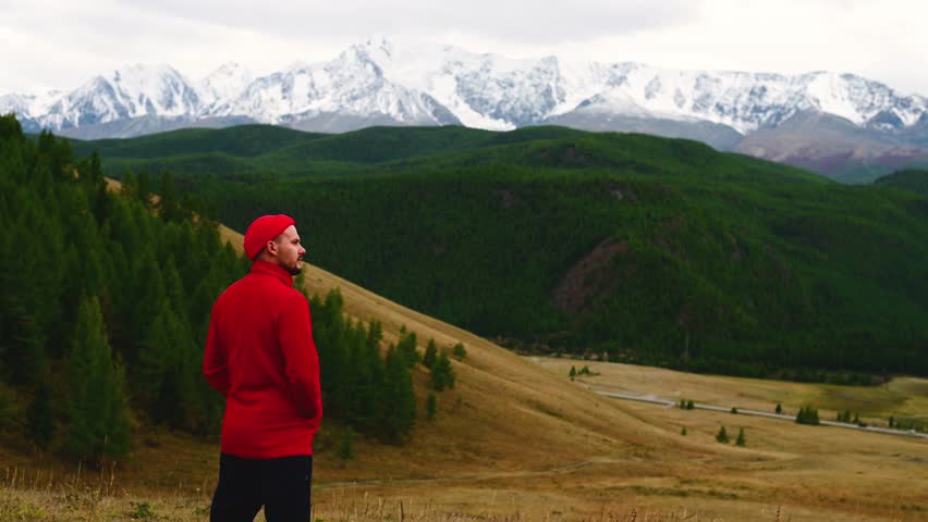 a guy in a red jacket stands against the background of the Chuisky ridge in Altai and looks at the mountains
