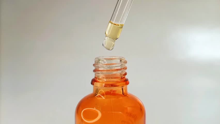 Close up bottle pipette dropper liquid yellow-orange vitamin c or retinol serum on white background.