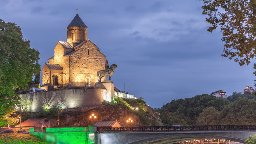 Metekhi Virgin Mary Assumption Church day to night transition timelapse and the Statue of King Vakhtang Gorgasali above the Kura River after sunset. Traffic on a bridge. Tbilisi, Georgia.