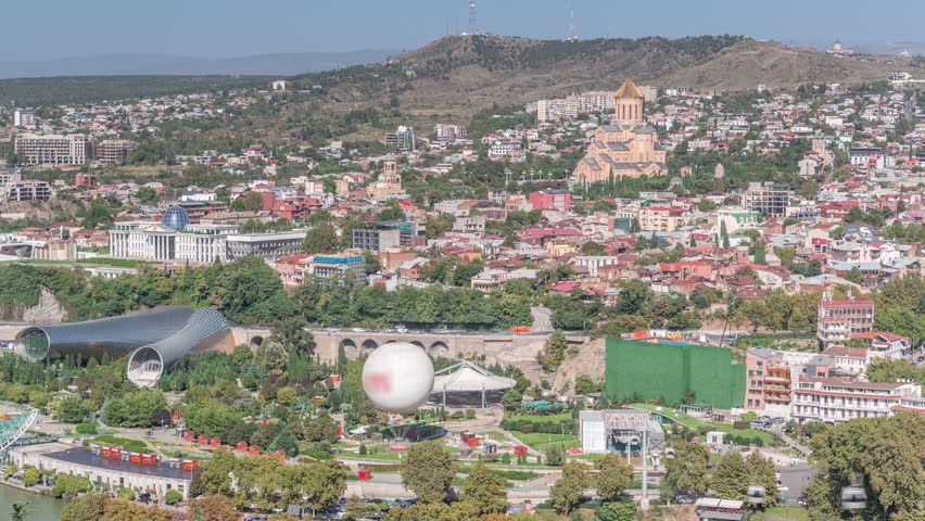 Holy Trinity Cathedral of Tbilisi, the Ceremonial Palace of Georgia and concert hall in Rike Park aerial timelapse panorama. Tbilisi, Georgia. Houses on a background and traffic on a road