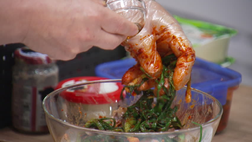 Mixing sesame oil with green onion kimchi in a glass bowl